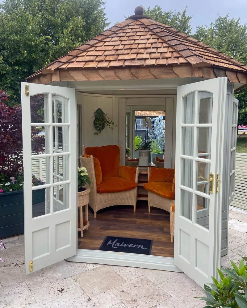 Woven armchairs with orange cushions inside an open garden summerhouse